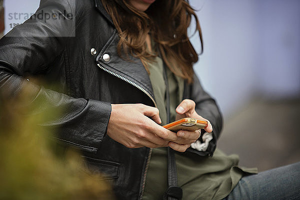 Mittelsektion einer Frau  die ein Mobiltelefon benutzt  während sie sich im Freien ausruht
