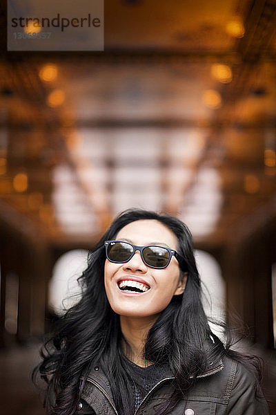 Frau mit Sonnenbrille lacht  während sie im Freien steht