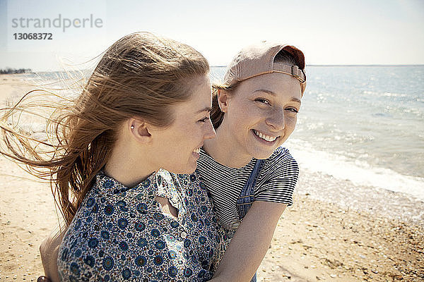 Porträt einer glücklichen Frau  die einen Freund umarmt  während sie am Strand steht