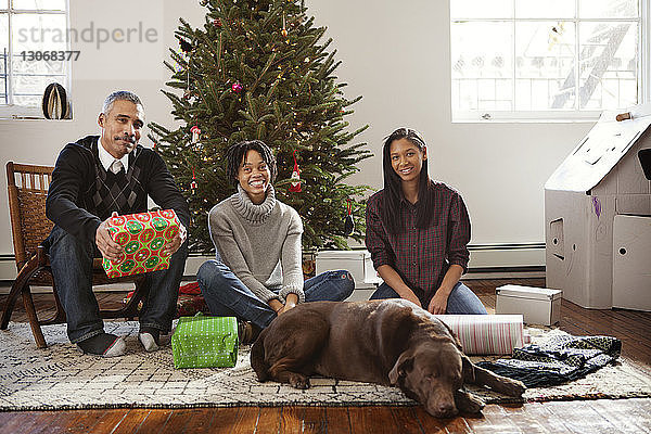 Glückliche Familie mit Hund sitzt zu Hause am Weihnachtsbaum