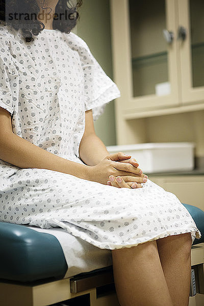 Mitschnitt einer Frau mit gefalteten Händen  die im Krankenhaus auf dem Bett sitzt