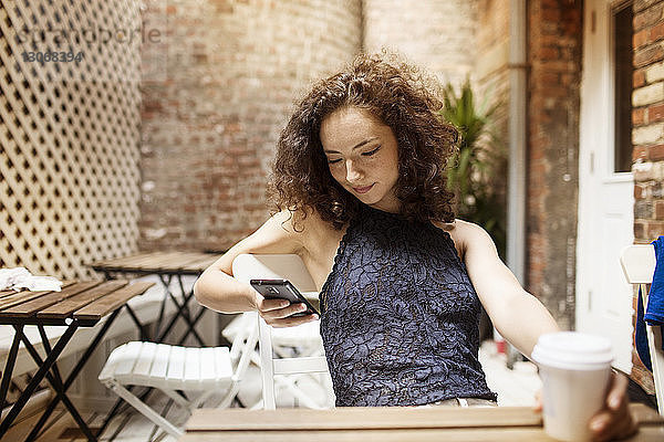 Frau benutzt Telefon  während sie im Straßencafé sitzt