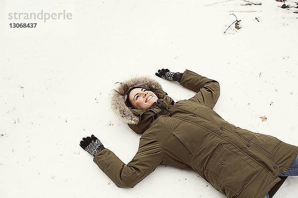 Hochwinkelaufnahme einer glücklichen Frau  die auf einem Schneefeld liegt