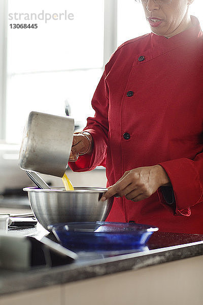 Mittelteil einer Frau  die während der Zubereitung einer Torte Flüssigkeit in einen Behälter gießt