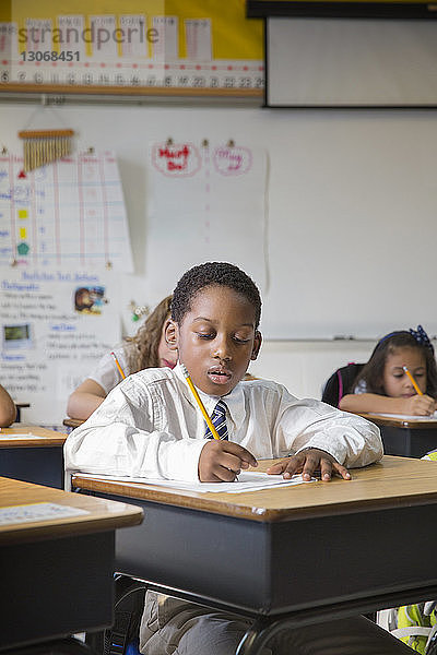 Junge schreibt auf Papier  während er im Klassenzimmer am Schreibtisch sitzt