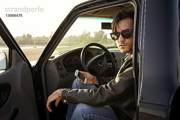 Porträt eines Mannes  der ein Smartphone in der Hand hält  während er im Auto sitzt