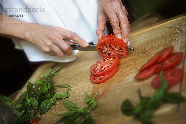 Beschnittenes Bild einer Frau  die auf einem Schneidebrett Tomatenscheiben nach Minzblättern schneidet