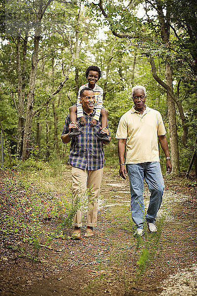 Mann trägt Sohn auf den Schultern  während er mit Vater im Wald spazieren geht