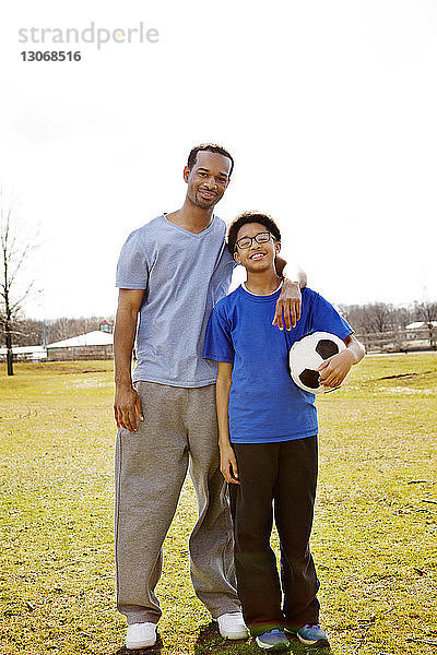 Porträt von Vater und Sohn mit Fussball auf dem Feld vor klarem Himmel stehend