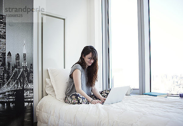 Lächelnde Frau benutzt Laptop-Computer  während sie zu Hause im Bett sitzt