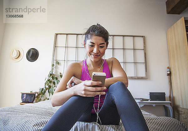 Lächelnde sportliche Frau hört Musik über Smartphone im Schlafzimmer