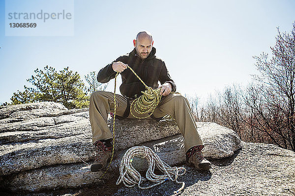 Wanderer mit Seil  der sich zum Abseilen vorbereitet  während er auf Felsen vor klarem Himmel sitzt