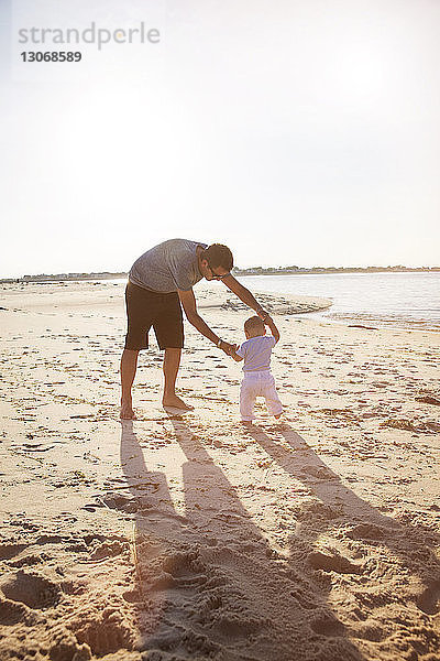 Vater und Sohn spielen an der Küste am Strand gegen den klaren Himmel