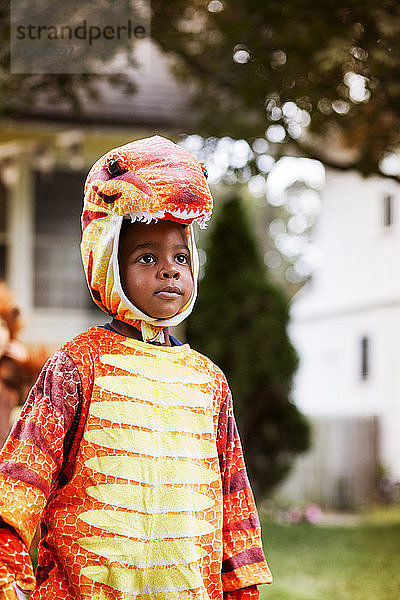 Süßer Junge in Dinosaurier-Kostüm steht an Halloween im Hof