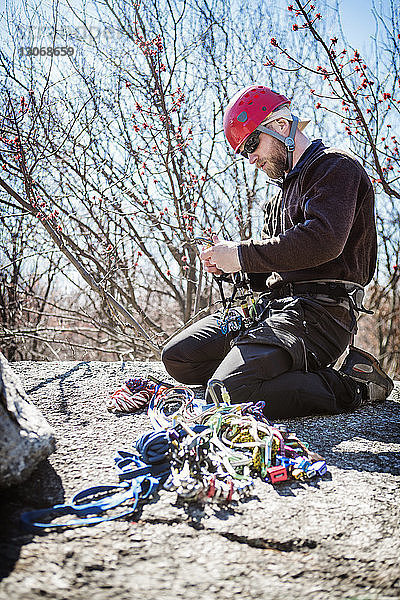 Seitenansicht eines Mannes  der sich auf Felsen kniend auf das Abseilen vorbereitet