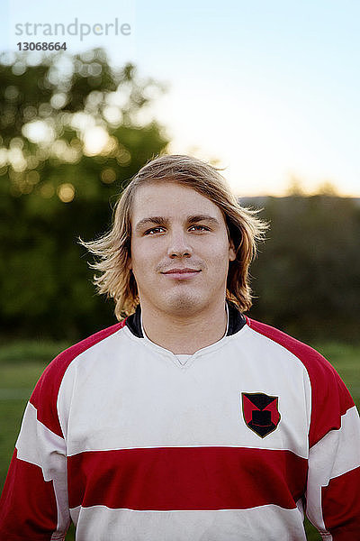 Selbstbewusster Rugby-Spieler steht auf dem Feld gegen den Himmel