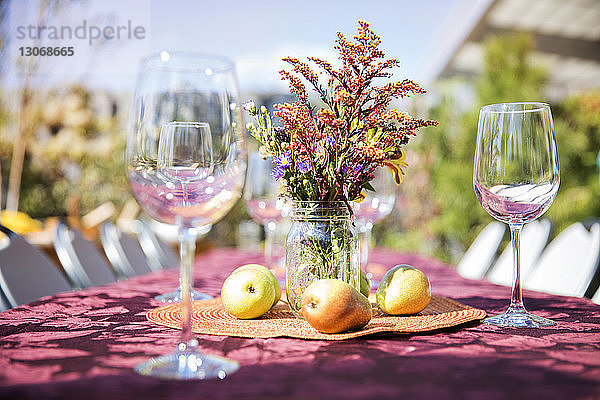 Leere Weingläser mit Früchten und Blumenvase auf Außentisch bei Gartenparty