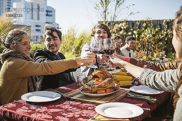 Freunde stoßen während der Gartenparty an einem Tisch im Freien auf rote Weingläser an