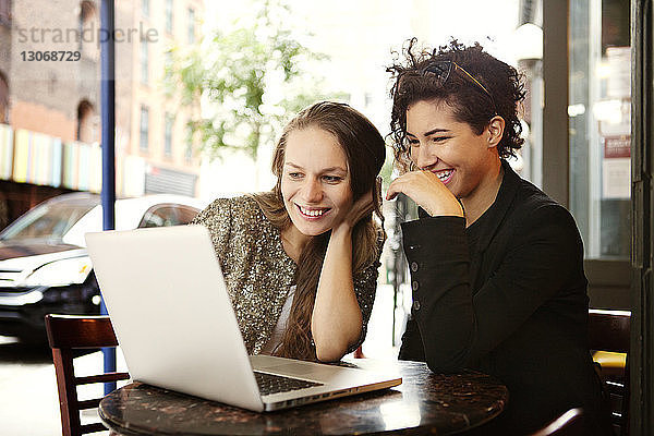 Freunde benutzen Laptop-Computer  während sie im Straßencafé sitzen