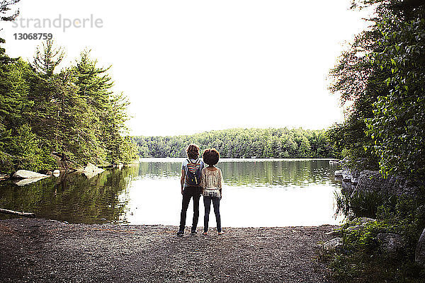 Rückansicht eines Paares  das den See betrachtet  während es auf einem Felsen vor klarem Himmel steht