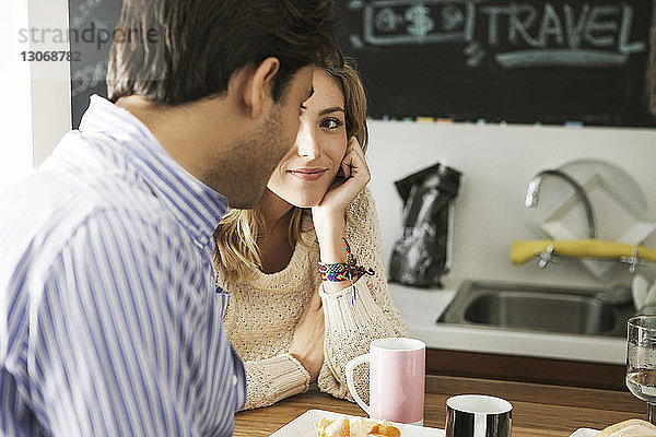 Frau sieht Mann an  während sie sich in der Küche an den Tisch lehnt
