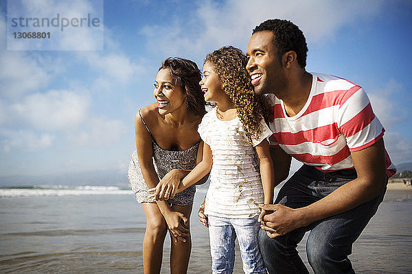 Glückliche Familie schaut weg  während sie am Strand am Ufer steht