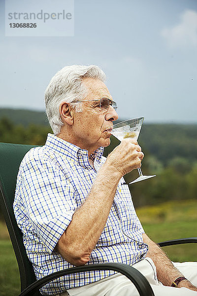Älterer Mann trinkt Martini  während er auf einem Stuhl im Rasen sitzt