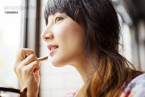 Frau schaut weg  während sie Lippenstift aufträgt