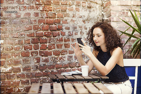 Frau benutzt Mobiltelefon  während sie im Straßencafé sitzt