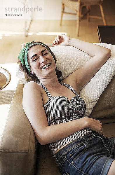 Hochwinkelansicht einer glücklichen Frau  die sich zu Hause auf dem Sofa entspannt