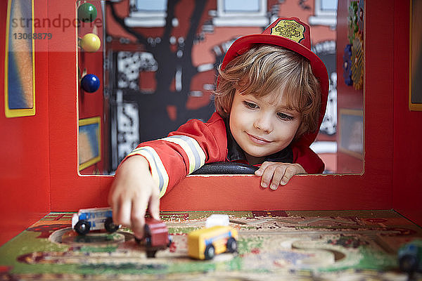 Lächelnder Junge als Feuerwehrmann verkleidet  der im Kindergarten mit Spielzeugautos spielt