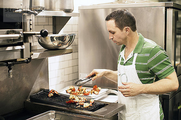 Mann bereitet Essen am Grill in einer Großküche zu