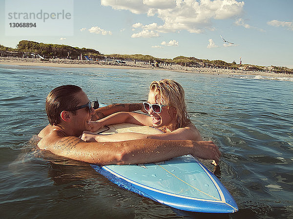 Paar lehnt am Strand auf einem Surfbrett