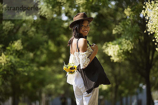 Porträt einer lächelnden Frau mit Umhängetasche im Park stehend