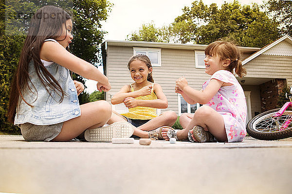 Mädchen spielen  während sie auf der Straße gegen ein Haus sitzen