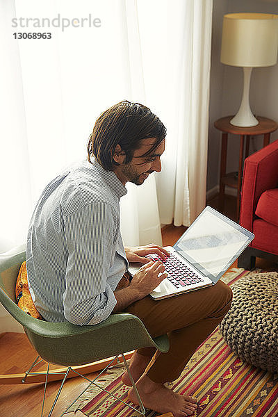 Hochwinkelansicht eines Mannes  der bei der Benutzung eines Laptops zu Hause wegschaut