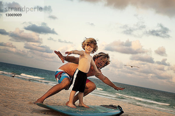 Porträt eines Vaters  der seinem Sohn das Surfen am Strand beibringt
