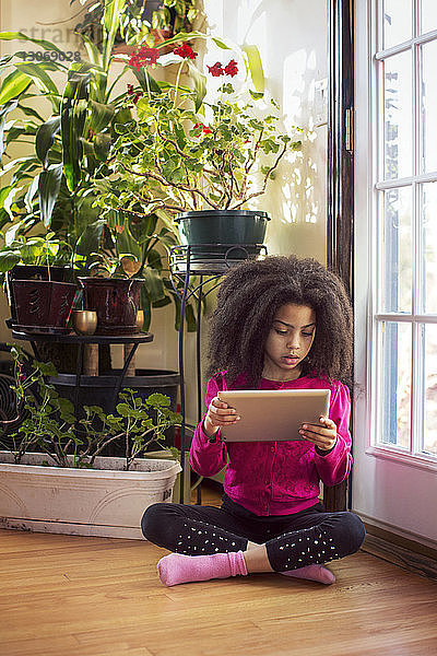 Mädchen benutzt einen Tablet-Computer  während sie zu Hause am Boden vor der Tür sitzt