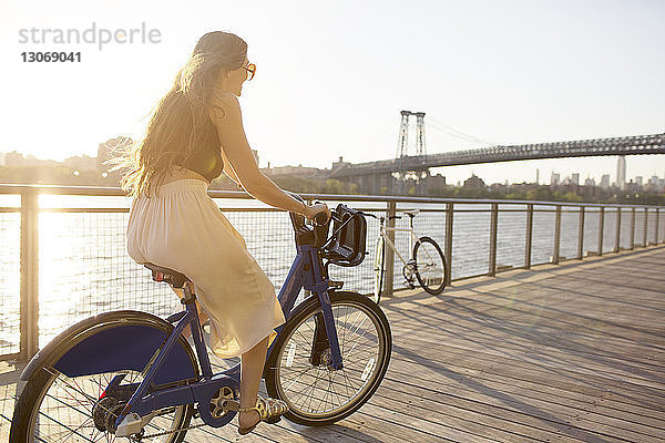 Glückliche Frau fährt bei Sonnenuntergang Fahrrad auf der Promenade