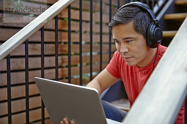 Mann hört Musik über einen Laptop-Computer  während er auf einer Treppe sitzt