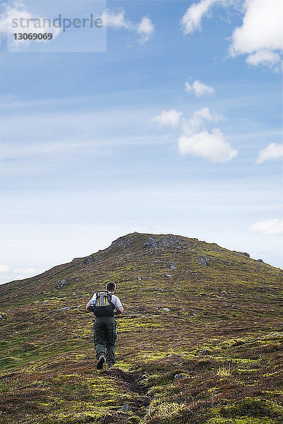 Rückansicht eines Mannes mit Rucksack beim Wandern auf einem Berg gegen den Himmel