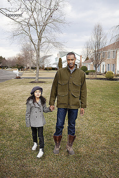 Porträt eines Vaters und einer Tochter  die sich an den Händen halten  während sie im Hinterhof stehen