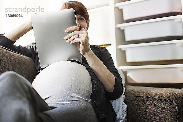 Schwangere Frau benutzt Tablet-Computer  während sie sich zu Hause auf dem Sofa entspannt