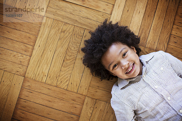 Porträt eines glücklichen Jungen auf Holzboden liegend