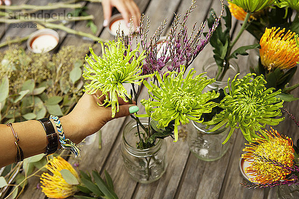 Ausgeschnittenes Bild einer Frau  die Blumen in Gläsern auf dem Tisch arrangiert