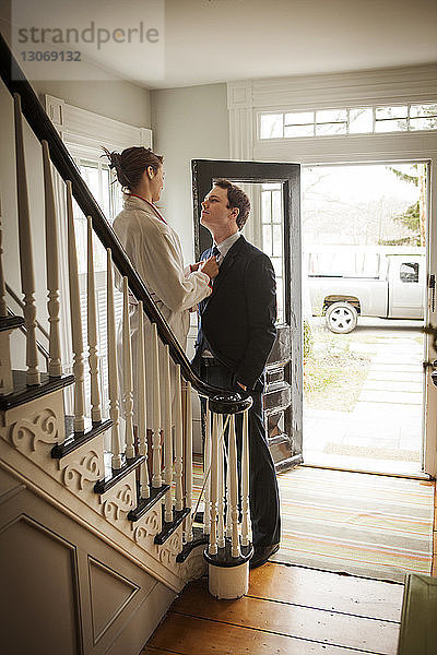 Frau justiert die Krawatte des Mannes  während sie zu Hause auf der Treppe steht