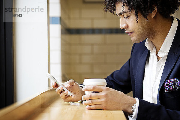 Seitenansicht eines Mannes  der ein Mobiltelefon benutzt  während er im Café sitzt