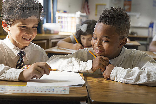 Lächelnde Studenten lernen  während sie im Klassenzimmer am Schreibtisch sitzen