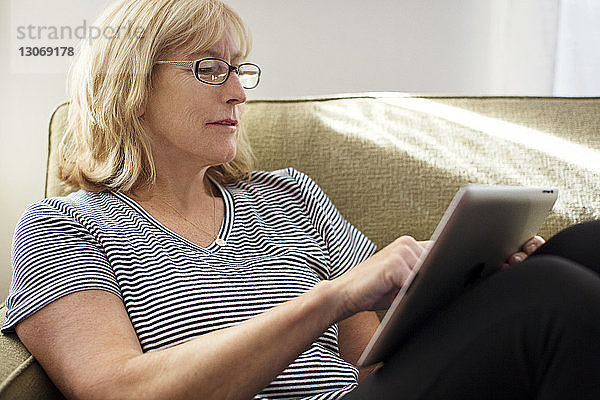 Nahaufnahme einer Frau  die einen Tablet-Computer benutzt  während sie zu Hause auf dem Sofa sitzt