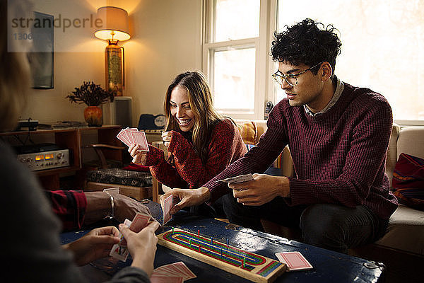 Fröhliche Freunde spielen Karten  während sie sich im beleuchteten Wohnzimmer ausruhen